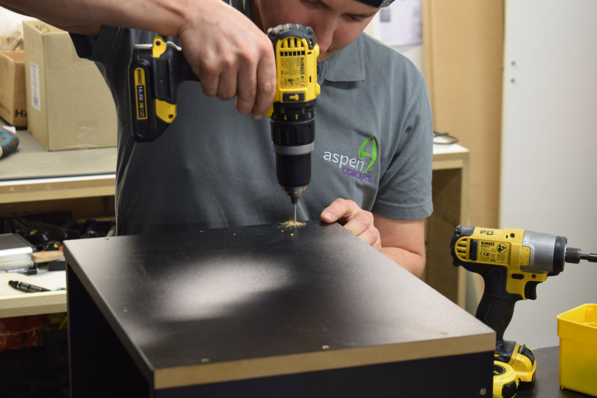 man drilling a hole in Aspen Concepts branded workwear